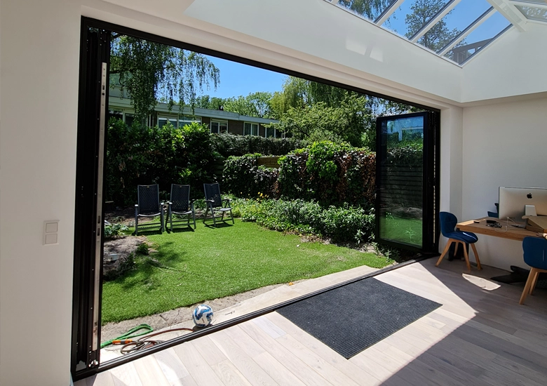 Moderne woning in Amsterdam met volledig geopende aluminium vouwdeuren (harmonicadeuren) van Reynaers, slanke profielen en naadloze overgang tussen binnenruimte en tuin